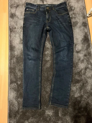 Mörkblå slim fit jeans  - Snygga mörkblå slim fit jeans från Zara med klassisk femficksdesign och kontrastsömmar. Jeansen har en rak passform och är tillverkade i stretchigt denimtyg för extra komfort. Perfekta för en avslappnad och trendig look.w33 L32