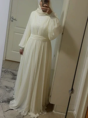 Vit långklänning med vida ärmar - Elegant vit långklänning med plisserad kjol och vida, långa ärmar. Klänningen har markerad midja med bredt band och hög halsringning. Tunt, flytande tyg som ger ett drömmigt intryck. Perfekt för dig som gillar en modest och stilren look. Den var gjord custom made i Turkiet, haft på mig den i ett bröllop en gång och kemtvättat. För fler bilder skriv gärna 💕