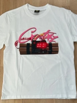 Vit t-shirt med grafiskt tryck - Vit t-shirt med ett stort grafiskt tryck på bröstet som föreställer en tecknad bomb med digital timer och rosa graffiti-text. T-shirten har rund hals och korta ärmar, perfekt för en streetwear-look.