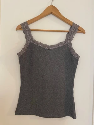 Grå ribbad linnetopp med spets - Snygg grå ribbad linnetopp med breda axelband och dekorativ spets längs ringningen och banden. 