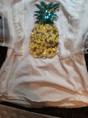 En unik top från yu&me - Very uniquely designed with eye-catching patterns at the front by the arms... this white t-shirt with its sparkling glittered pineapple will make your day in any boring urban jungle... Perfect for spring or summer. In excellent condition. 