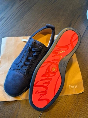 Svarta Christian Louboutin sneakers - Snygga svarta sneakers från Christian Louboutin i mocka med klassisk röd sula och svarta skosnören. Låg modell med rund tå och diskreta sömdetaljer. Perfekta för dig som vill ha något exklusivt och stilrent.