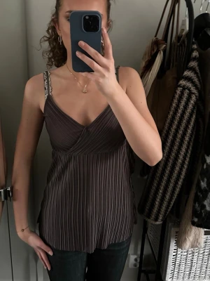 Brun omlott linnetopp med smala axelband - Säljer en brun omlott linnetopp med smala axelband och plisserad struktur. Toppen har v-ringning och en loose passform, perfekt för en trendig och avslappnad look.