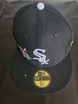 Svart White Sox keps från New Era - Snygg svart keps från New Era med White Sox-logga broderad framtill och blommigt motiv på sidan. Patch med '1933 All Star Game Chicago' på sidan. Flat skärm och klassisk 59FIFTY-modell. Perfekt för dig som gillar sport och streetstyle.