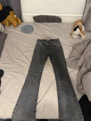 Grå bootcut jeans  - Säljer ett par grå bootcut jeans med klassisk femficksdesign. Jeansen har en snygg tvättad look och är tillverkade i denim med stretch för skön passform. Perfekta för dig som gillar en avslappnad och trendig stil.
