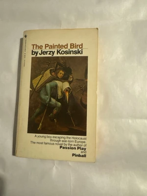 The Painted Bird av Jerzy Kosinski - Säljer romanen 'The Painted Bird' av Jerzy Kosinski, engelsk pocketbok med vit omslag och surrealistisk konst på framsidan. Boken handlar om en ung pojkes flykt genom krigets Europa under Förintelsen. Perfekt för dig som gillar starka berättelser och klassisk litteratur.