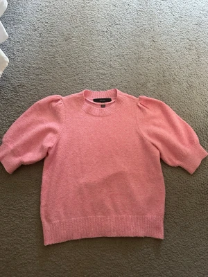 Rosa stickad tröja från Vero Moda - Söt rosa stickad tröja från Vero Moda med korta ärmar och ribbstickade muddar vid hals, ärmslut och nederkant. Ärmarna är lite puffiga och ger en fin look. Tröjan är i ett lätt och mysigt material. Storleken är XS och passar bra i passform. 