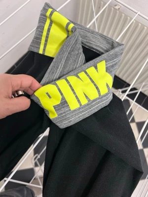 Svarta pant  från PINK med grå midja - Snygga svarta pants yoga  från PINK Victoria secrets med bred grå midjeresår och neon-gula detaljer samt stor logga . Perfekta för träning eller chill, stretchigt material som sitter skönt och markerar midjan. Midjebandet har två gula ränder och texten PINK i gult.