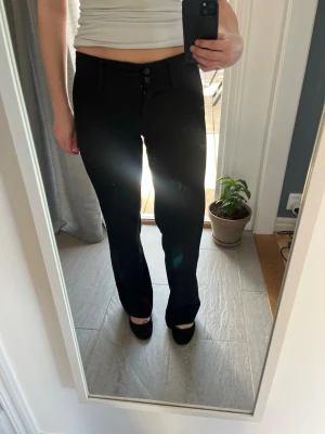 Svarta kostymbyxor med raka ben - Snygg svart lågmidjad kostymbyxa med raka ben och två knappar framtill. Säljer då de tyvärr har blivit försmå 