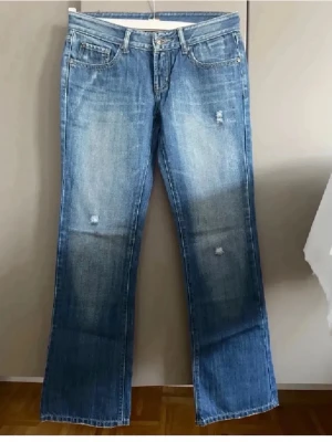 Blå jeans med slitningar  - Snygga blå  jeans med lätt slitna detaljer framtill och klassisk femficksdesign. Bakfickorna har dekorativa sömmar i gult. Jeansen har normal midja och stängs med dragkedja och knapp. Perfekta för en avslappnad och trendig look.