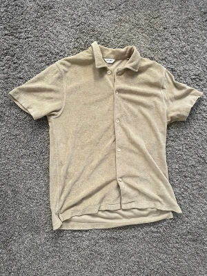 Beige frottéskjorta med kort ärm - Snygg beige skjorta  i mjuk frotté. Skjortan har korta ärmar, klassisk krage och knäppning framtill. Perfekt för en avslappnad och trendig look.