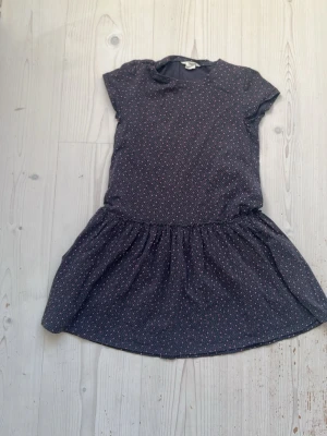 Mörkgrå kortärmad klänning med små rosa hjärtan. - Söt mörkgrå klänning med små rosa hjärtan , rund hals och korta ärmar. Kjolen är lätt utställd och klänningen har en lös passform. Är från H&M och är  134/140.