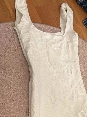 Vit lång klänning med breda axelband - Säljer en elegant vit lång klänning med breda axelband och rundad urringning. Klänningen har en slät, lätt utformad yta och figurnära passform som ger en stilren look. Perfekt för dig som vill ha en enkel men snygg outfit. Använd en gång. Pris kan alltid diskuteras