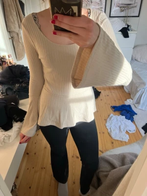 Ribbad beige topp med utsvängda ärmar - Superfin ribbad topp från Lindex i beige med utsvängda långa ärmar och rund halsringning. Toppen har en lätt figursydd passform och är tillverkad i mjukt material som känns skönt mot huden. Perfekt att styla med jeans eller kjol.
