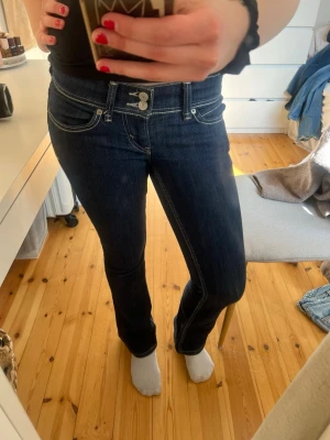 Super low waist bootcut jeans från Levis - Säljer ett par mörkblå bootcut jeans från Levis med dubbla knappar i midjan och vita kontrastsömmar. Klassisk femficksmodell och låg midja. Snygga detaljer och stretchigt denimtyg som sitter riktigt bra.