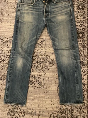 Blå raka jeans med slitningar - Säljer ett par blå jeans med raka ben och tydliga slitningar framtill och baktill. Jeansen har klassiska fem fickor och kontrastsömmar. Materialet är denim i bomull och de har en avslappnad, vintage look. Märket är G-star Raw. Storlek: 33/32, kom priv om du har fundering! Kan sänka pris vid snabb affär!
