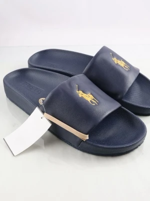 Marinblå slides från Polo Ralph Lauren - Snygga marinblå slides från Polo Ralph Lauren med klassisk gul broderad logga på ovandelen. Tillverkade i syntetmaterial med räfflad sula för extra grepp. Perfekta för chill dagar och enkel att matcha med olika outfits. Herr. Varan är begagnad och defekter kan förekomma men nästan intill som nyskick. Storlek 42 och pris kan diksuteras 