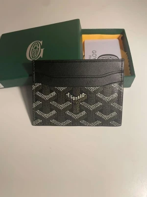 Svart kortfodral från Go4yard - Säljer ett stilrent svart kortfodral från Go4yard med deras ikoniska mönster i vitt och grått. Fodralet är tillverkat i läder och har flera kortfack. Perfekt för dig som vill ha en lyxig och smidig plånbok i fickan.