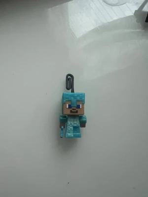 Kinder joy - Minecraft nyckelring med diamantgubbe - Nyckelring med en figur från Minecraft som har blå diamantutrustning och svärd. Figuren är fyrkantig och gjord i plast, med en svart ögla för att fästa på nycklar eller väska. Perfekt för fans av spelet.