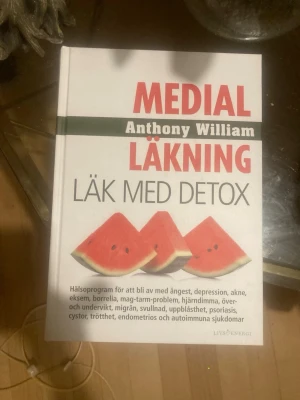 Medial Läkning: Läk med detox - Boken 'Medial Läkning: Läk med detox' av Anthony William är en inbunden bok med vit framsida och röda samt svarta texter. Omslaget har bilder på vattenmelon och boken innehåller hälsoprogram och detoxråd för olika sjukdomar och besvär.