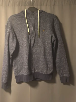 Mörkblå hoodie med halv dragkedja - Mörkblå hoodie med halv dragkedja framtill och ljusa snören i huvan. Tröjan har ribbade muddar vid ärmslut och nederkant samt en liten logga på bröstet. Materialet är mjukt och bekvämt, perfekt för chill dagar. Klassisk passform och stilren look.