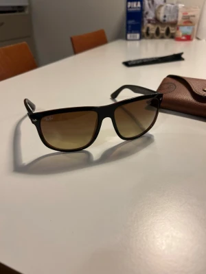 Ray-Ban Boyfriend - Snygga Ray-Ban solglasögon med svart båge och bruna tonade glas. Klassisk rektangulär form som ger en cool vibe. Kommer med original Ray-Ban-fodral i brunt skinn. Perfekta för soliga dagar och en stilren look.