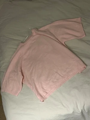 Ljusrosa stickad tröja - Söt ljusrosa stickad tröja med rund hals och trekvartsärmar. Tröjan har en avslappnad passform och ribbstickade muddar vid ärmslut och nederkant. Perfekt för lager på lager och enkel att styla till olika outfits.