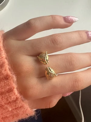 Guldfärgad ring med leopardhuvuden - Cool ring i guldfärgad metall med två detaljerade ormhuvuden som möts framtill. Ringen har en öppen design och fina ingraverade detaljer på ormarna. Vet ej vad det är för material exakt. Hör av dig vid frågor💕 Den är justerbar så den passar alla!!