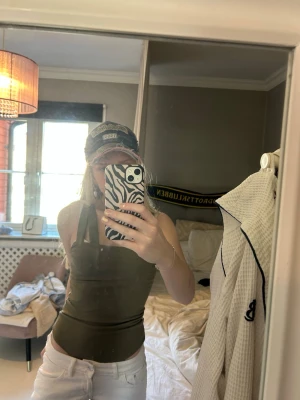 Olivgrön body - Säljer en olivgrön body med breda axelband och tight passform. Toppen har en enkel, stilren design och är perfekt att matcha med jeans eller kjol. Materialet känns mjukt och stretchigt, vilket gör den bekväm att bära hela dagen.