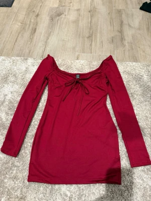Vinröd långärmad klänning Shein - Supersnygg vinröd klänning från Shein med lång ärm och söt snörning framtill. Klänningen har en figurnära passform och offshoulder-design som ger en trendig look. Perfekt för dig som vill sticka ut lite extra. Lite öppen i ryggen och man kan ha den på två olika sätt. 