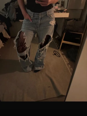 Ljusblå slitna baggy jeans - Säljer ett par ljusblå baggy jeans med stora slitningar över knäna och lös passform. Jeansen har hög midja, fem fickor och klassisk knappgylf. Perfekta för en avslappnad och trendig streetstyle-look.