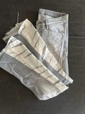 Grå jeans med vita detaljer - Säljer ett par jättefina gråa jeans med zebra bootcut som jag sytt. Längden 95 cm, innebenslängd 74 cm och midjemått 72 cm. 