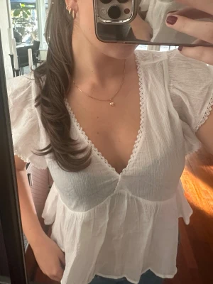 Vit blus med volang och spetsdetaljer - Söt vit blus med v-ringning, volang nedtill och spetskant längs urringningen. Luftigt material och korta, fladdriga ärmar. Från Nelly i storlek 38, aldrig använd💕