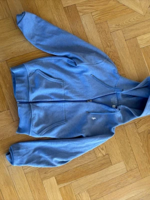 Blå hoodie från Polo Ralph Lauren - Snygg blå hoodie från Polo Ralph Lauren med dragkedja framtill och två stora fickor. Klassisk broderad logga på bröstet och justerbar huva. Tillverkad i mjuk bomullsblandning som känns skön mot huden. Perfekt för en avslappnad och stilren look. Väldigt fint skick och är sparsamt använd. Kontakta gärna om ni har några frågor😃