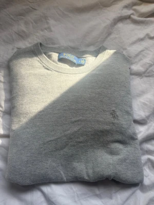 Polo Ralph Lauren cashmere - Snygg grå tröja från Polo Ralph Lauren med rund halsringning och diskret broderad logga på bröstet. Tillverkad i mjukt material som passar perfekt till lager på lager eller som den är. Klassisk och stilren design.