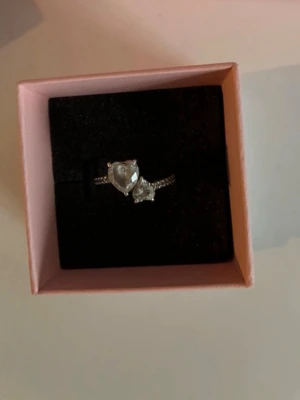 Silverring med hjärtformad sten Pandora - Säljer en elegant silverring från Pandora med två hjärtformade klara stenar framtill. Ringen har en tunn banddesign med små gnistrande stenar längs sidorna. Kommer i originalask från Pandora. Size S