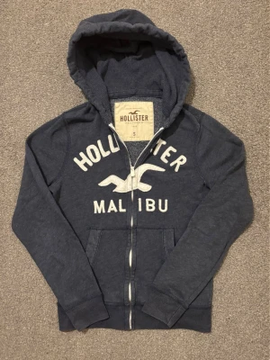 Vintage Hollister Zip-Hoodie - Sjukt fet Hollister zip hoodie som är mycket eftertraktad | Mycket bra skick, snören fattas | Storlek S | Längd ≈ 64cm , Bredd armhåla-armhåla ≈ 54cm | Modell 175cm, 68kg | Hör av vid funderingar!