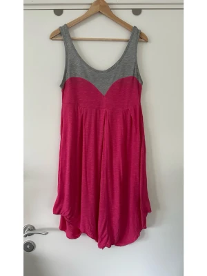 Grå och rosa hjärtformad Gina Tricot klänning, storlek L - Charmig klänning från Gina Tricot i storlek L med grå axelband och rosa / fuchsiafärgad hjärtformad byst- och kjoldel. Överdelen har breda axelband och en rundad halsringning. Vid kjol med bekväm lös passform. Mycket gott skick!