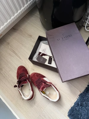 Vinröda sneakers från Valentino - Snygga vinröda sneakers från Valentino med vita detaljer och klassisk låg siluett. Skorna är tillverkade i mocka och har matchande vinröda skosnören samt vit sula. Perfekta för dig som vill ha en stilren och exklusiv look. Öppen för byten också 🤩