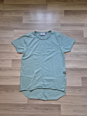 Ljusgrön t-shirt med ficka - Snygg ljusgrön t-shirt från Denim Day med rund halsringning och liten bröstficka. T-shirten har korta ärmar och längre, rundad nederkant både fram och bak. Perfekt för en avslappnad och trendig stil.