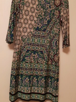 Blommig kortklänning från Wallis - Färgstark kortklänning från Wallis med blommigt mönster i grönt, blått, vitt och brunt. Klänningen har trekvartsärm och rund halsringning. Tillverkad i mjukt och stretchigt material, perfekt för dig som gillar retrovibbar och unika prints.