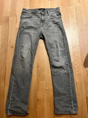 Grå raka jeans från replay - Säljer ett par grå jeans från replay med rak passform och klassiska fem fickor. Jeansen har en diskret tvättad look och replay’s ikoniska läderpatch bak i midjan. Materialet är slitstark denim i bomull. Perfekta till en avslappnad streetstyle.
