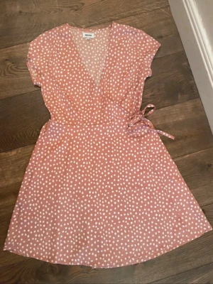 Rosa prickig omlottklänning Bubbleroom - Söt rosa kortklänning från Bubbleroom med vita prickar och omlottmodell. Klänningen har korta ärmar, knyt i midjan och v-ringad hals. Perfekt för sommarens alla tillfällen och ger en fräsch och trendig look.