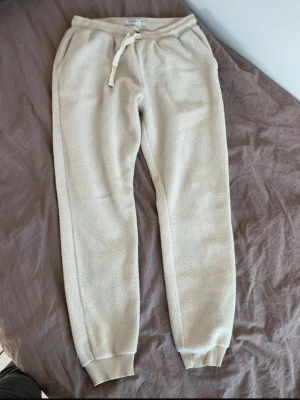 Beiga fleece-mjukisbyxor Les Deux - Mysiga beiga mjukisbyxor från Les Deux i storlek S. Tillverkade i mjuk fleece med resår och dragsko i midjan samt ribbade muddar vid bensluten. Perfekta för chill dagar hemma eller när du vill ha det extra bekvämt nypris kostar 1099kr.  