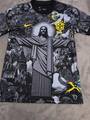 Nike Brasil Neymar JR tröja svart/gul - Unik svart Brasilien-tröja från Nike med Neymar JR och nummer 10 på ryggen. Framsidan har ett detaljerat tryck av Kristusstatyn och brasilianska motiv i gråskala, med gula och blå detaljer samt Brasil-logga. Perfekt för dig som älskar fotboll och vill sticka ut.