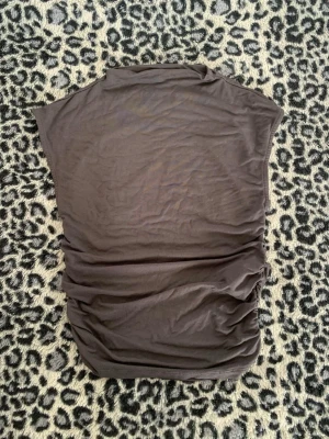 Mörkbrun ärmlös topp - Snygg mörkbrun topp i mjukt material med ärmlös design och lätt rynkade sidor. Perfekt att styla med jeans eller kjol för en trendig look.