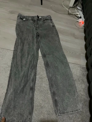 Gråa raka jeans med tvättad look - Säljer ett par gråa jeans med rak passform och tvättad, lite vintage-inspirerad look. Jeansen har hög midja och klassiska fem fickor. Perfekta för en avslappnad och trendig stil.
