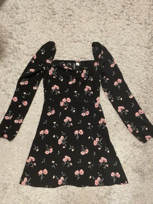 Blommig klänning från H&M – strl 36, aldrig använd  - Säljer denna sjukt fina svarta klänning med rosa blommor från H&M 🌸 Den sitter verkligen jättefint på kroppen med sin passform och lite puffiga axlar, ger en sån soft men ändå cute vibe yäni 😍 Perfekt till fest, middag eller bara när du vill känna dig extra fin.  Den är helt ny och aldrig använd, så den är i toppskick. Säljer bara för att den inte kommit till använd och förtjänar att bli buren istället 💅  Hör av dig om du undrar något 💌