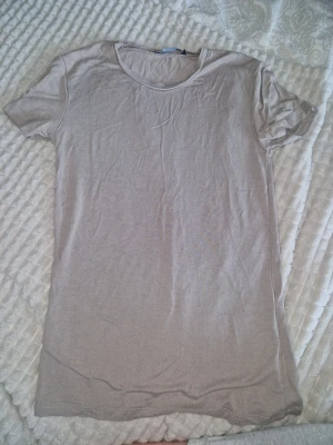Beige basic t-shirt i bomull lager 157 - En enkel och stilren beige t-shirt med rund hals och korta ärmar. Tillverkad i mjuk bomull som känns skön mot huden. Perfekt att matcha med jeans eller shorts för en clean look.