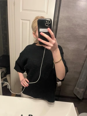 Svart oversized stickad tröja - Säljer en svart oversized stickad tröja med halvlånga ärmar och rund hals. Tröjan har en avslappnad passform och är perfekt att slänga på sig för en chill look. Materialet ser mjukt och bekvämt ut, perfekt för lager på lager. Storlek L men passar mig ganska bra som har xs-s i storlek.